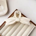 Close-up of a cream white matte bow hair claw clip on a minimalist display tray - White