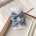 Detail of two dusty blue satin bow hair clips on a white display card with a jewelry box - Haze Blue
