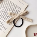 Detailansicht eines handgestrickten beigen Schleifenhaargummis mit Häkeltextur auf Buch - Khaki