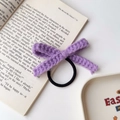 Detailaufnahme eines lila handgehäkelten Schleifen-Haargummis auf einem Buch - Lila