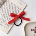 Detail eines handgestrickten orangefarbenen Haargummis auf einem offenen Buch mit Tablett - Rot