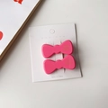Vue macro de deux barrettes nœuds rose brillant avec lettrage doré sur carte blanche - Rose
