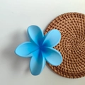 Sky blue plumeria flower hair claw clip with matte finish on woven beach mat background - Gradient Blue Matte
