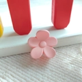 Nahaufnahme einer kleinen matten rosa Blumen-Haarklammer auf einem minimalistischen Ständer - Mädchenrosa - Matt