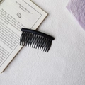 Detail view of a matte black curved hair comb placed on an open book for styling - Round Head Afro Comb / Black