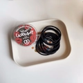 Close-up of durable black seamless hair elastics in a floral patterned container - Black Series