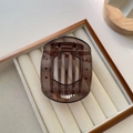 Detailed top view of large brown tortoiseshell hair claw clip on white velvet display tray - Large / Gray