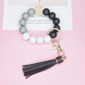 Minimalist beaded keychain with grey and black tassels on a pink backdrop background - Black