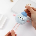 Elastic plush monster keychain with spring legs held by hand for stretch demonstration - Blue