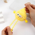 Detail of yellow plush monster keychain showing elastic spring legs being stretched by hand - Yellow