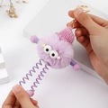 Close-up of purple plush monster keychain with spring legs and pink knitted hat details - Purple