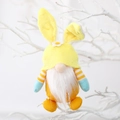 Easter gnome plush in yellow bunny ears with white daisy and orange vest hanging on branch - Yellow