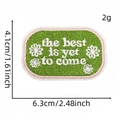 Green oval embroidered patch with The best is yet to come text and small white flowers - Colored English Letter Cloth Patch #18