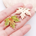 Detail of colorful enamel maple leaf pendant and textured rose gold charm held in hand - Large Green Enamel Thanksgiving Maple Leaf (25063)
