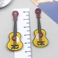 Detalle de dijes de guitarra en acrílico de colores con regla sobre fondo gris - Guitarra de Música Impresa a Doble Cara Amarilla (24047)
