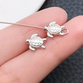 Zilveren zeeschildpad tussenkraal voor DIY-sieraden, getoond op een vingertop voor schaal - Schildpad Stijl (16369) / Antiek Zilver