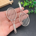 Detalle de dijes de raqueta de tenis plateados con textura de malla y diseño de empuñadura - Raqueta de Tenis de Plata Antigua