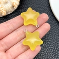 Detail showing two bright yellow resin star charms held on a textured leather background - Yellow Luminous Star (24066)