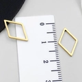 Dettaglio di ciondoli geometrici a rombo dorati su un righello per mostrare le misure - Oro