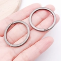 Close-up of two gunmetal flat split key rings with a matte finish on a palm - Gun Black Round Style (25821)