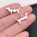 Set of two bright silver dachshund pendants for DIY jewelry making held by a hand - Bright Silver Dachshund 10x18mm (20538)