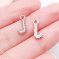 Silver letter J charms with rhinestones and engraved texture on person's palm - Letter J