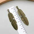 Detailed macro view of two bronze feather alloy charms measuring 5.5cm for DIY jewelry making - Antique Bronze (3241)