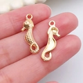 Golden seahorse alloy charms for DIY bracelets and necklaces shown on fingertips - 1Pc Seahorse 7x23mm