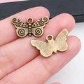 Gros plan d'un pendentif papillon en bronze vintage avec volutes pour la création de bijoux - Forme de Papillon 22x12mm (20159)