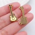 Zwei goldfarbene Gitarren-Anhänger für DIY-Schmuckherstellung in der Hand gehalten - Gitarreninstrument Stil