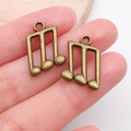 Close-up of bronze musical note pendants held between fingers for DIY jewelry scale - Triplet Note (20895)