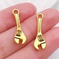 Golden alloy wrench-shaped charms for DIY jewelry making shown on hand palm - Wrench 24x7mm (20395)
