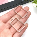 Two silver rectangle DIY pendants on hand showing scale and metallic texture - 21x30mm / White K Rectangular Frame (10474)