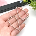 Silver geometric hollow frame charms for DIY jewelry making held in hand for scale - 21x40mm / White K Bullet Shape Frame (10477)