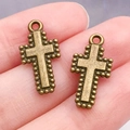 Dos colgantes de cruz de bronce antiguo para joyería DIY mostrados sobre la mano - Estilo Cruz (20325)