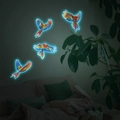 Adesivi murali luminosi con pappagalli colorati in volo e bagliore blu in una camera da letto - Blu
