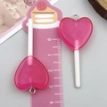 Gros plan de pendentifs sucettes cœur en résine rose pailletée avec règle de mesure - Sucette Cœur Transparent Rose Rouge (24557)