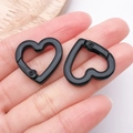 Close-up of heart-shaped matte black alloy spring clasp held by fingers for size - Black