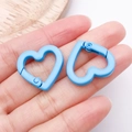 Close-up of light blue heart-shaped alloy spring clasps held by hand for scale - Blue