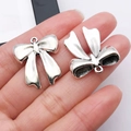Dettaglio dei ciondoli a fiocco argento nel palmo per la creazione di gioielli DIY - 24.5x22mm / Fiocco Argento Antico (26996)