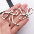 Dettaglio di ciondoli a fiocco in argento vintage per gioielli fai-da-te tenuti in mano - 42x42mm / Fiocco Cavo Argento Antico (26997)