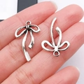 Ciondolo a fiocco argento vintage in lega per gioielli DIY, mostrato sulla mano per scala - 24.5x15mm / Fiocco Cavo Argento Antico (26991)