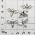 Macro detail of vintage silver bee charms with wing textures on a metric grid background - Bee Style (9186)