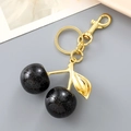 Macro detail of cherry bag charm featuring black glitter fruit and gold hardware - Black
