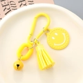 Detail of yellow smiley face keychain with leather tassel and bell in a ceramic dish - Yellow