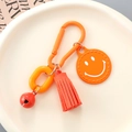 Detail of bright orange keychain with tassel, smiley face charm and metal bell on a tray - Orange