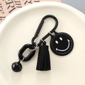 Black candy-colored smiley face keychain with metal links, tassel and bell on a plate - Black