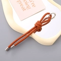 Handmade woven orange PU leather keychain with silver metal ring on a minimalist tray - Brown