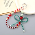 Macro shot of handmade strawberry bead phone charm with green crystal bow and silver clasp - Red