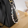 Detail of crystal beaded phone charm with silver butterfly pendant on a leather bag - White